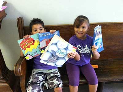 Two young children holding up various books they received through The Urban Mission.